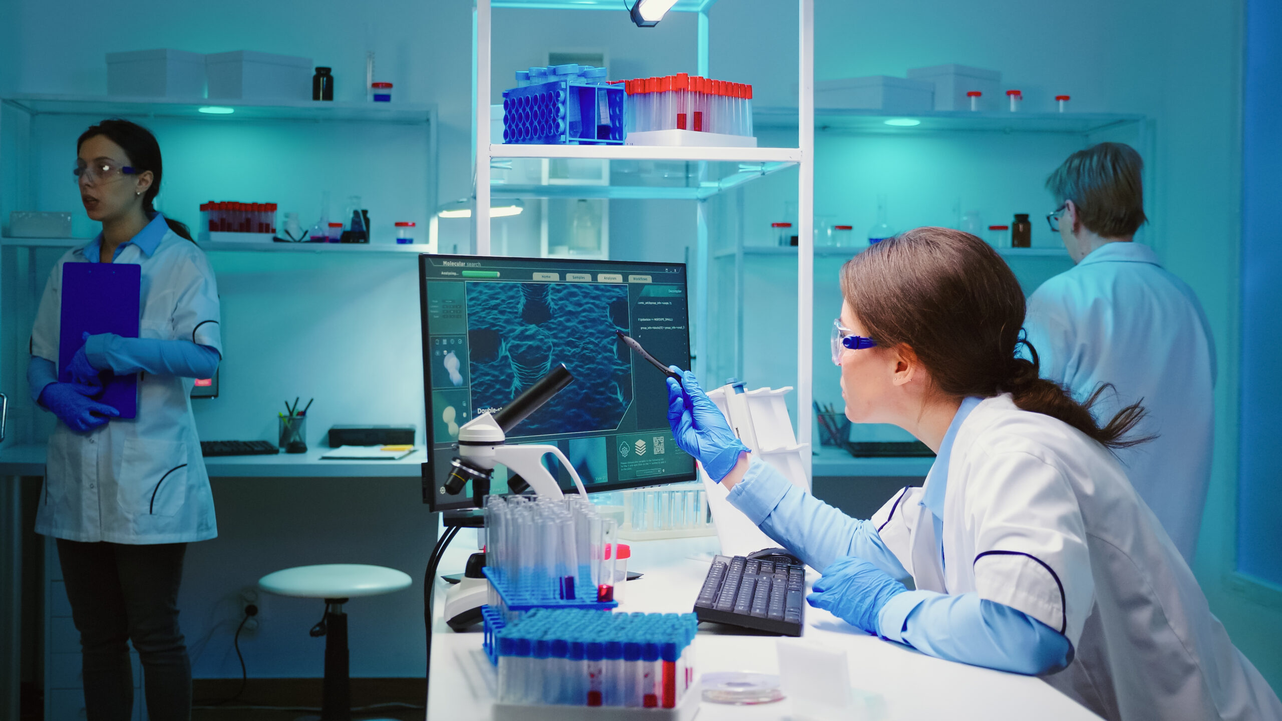 Woman biochemist checking manifestations of virus working on computer in equipped lab late at night. Team of doctors examining vaccine evolution using high tech researching diagnosis against covid19