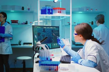 Woman biochemist checking manifestations of virus working on computer in equipped lab late at night. Team of doctors examining vaccine evolution using high tech researching diagnosis against covid19
